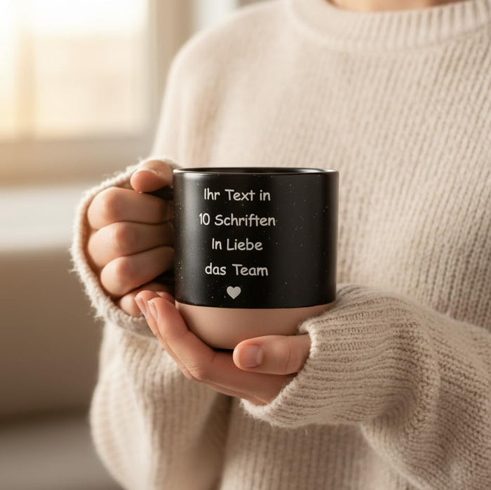 Frau hält schwarze personalisierte Tasse mit Gravur und Herz in beiden Händen