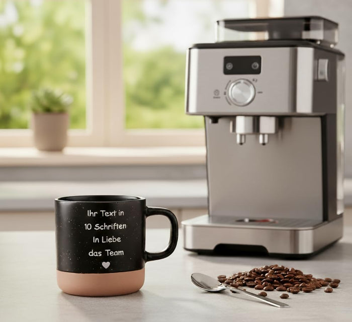 Schwarze personalisierte Kaffeetasse mit Gravur neben Kaffeevollautomat und Kaffeebohnen in heller Küche