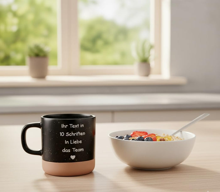 Schwarze Tasse mit Wunschgravur neben einer Müslischale mit Beeren am Frühstückstisch