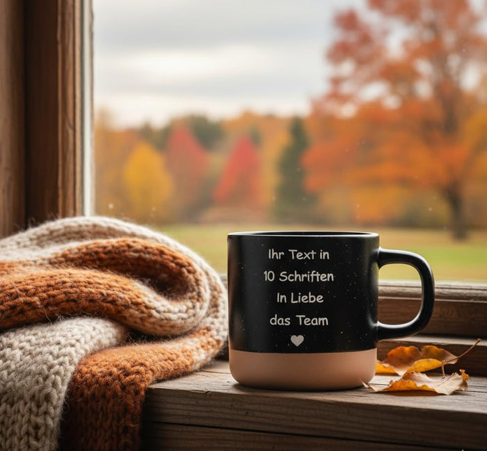 Schwarze Tasse mit Gravur auf einer Fensterbank mit Herbstlaub und Strickschal